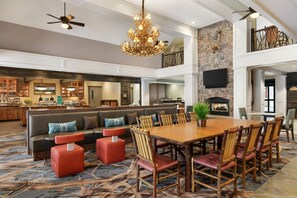 A spacious living area with a high ceiling, a fireplace, and a large dining table surrounded by chairs. - Homewood Suites by Hilton Syracuse/Liverpool (Liverpool)