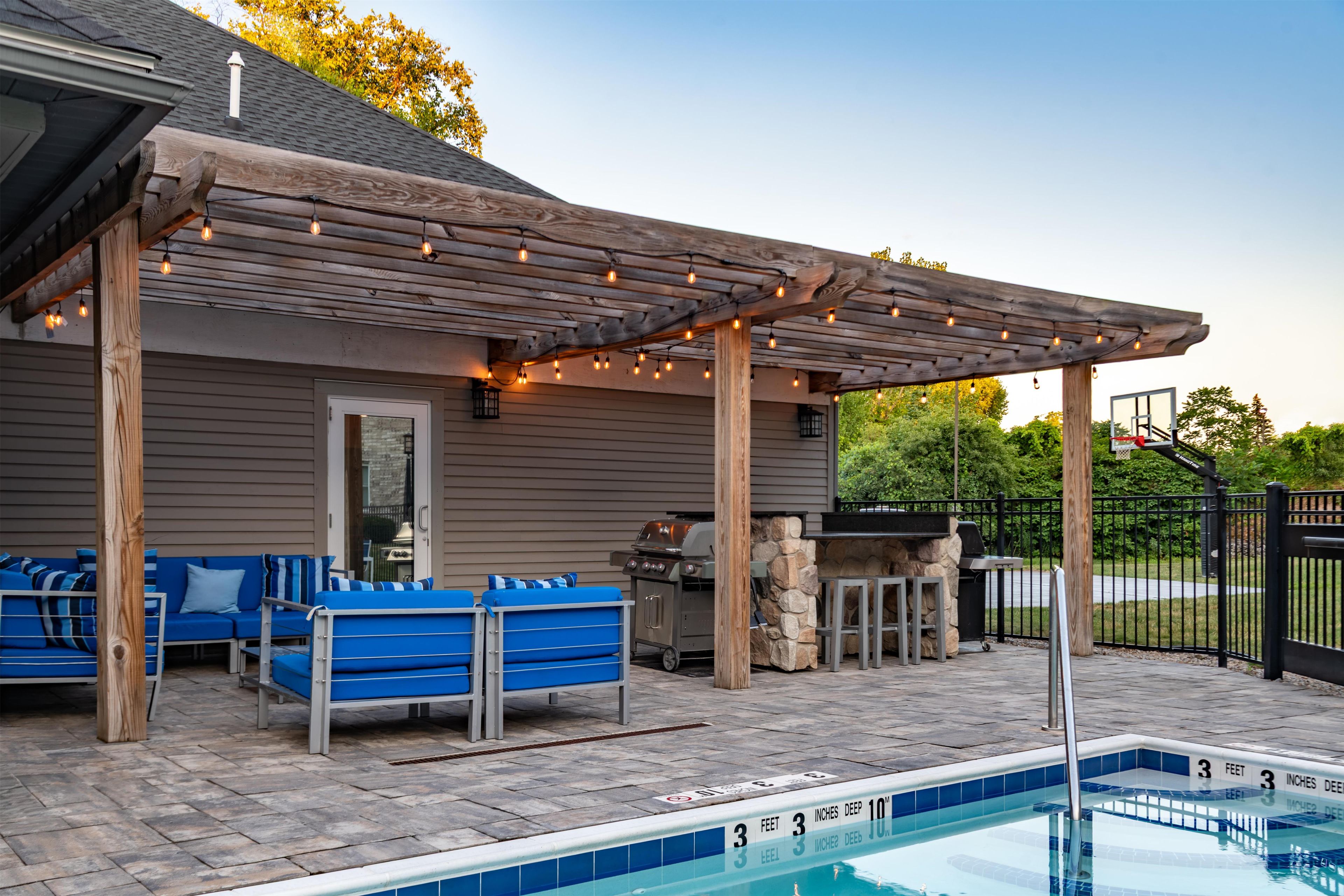 A poolside area with a covered seating area, a barbecue grill, and a stone wall.