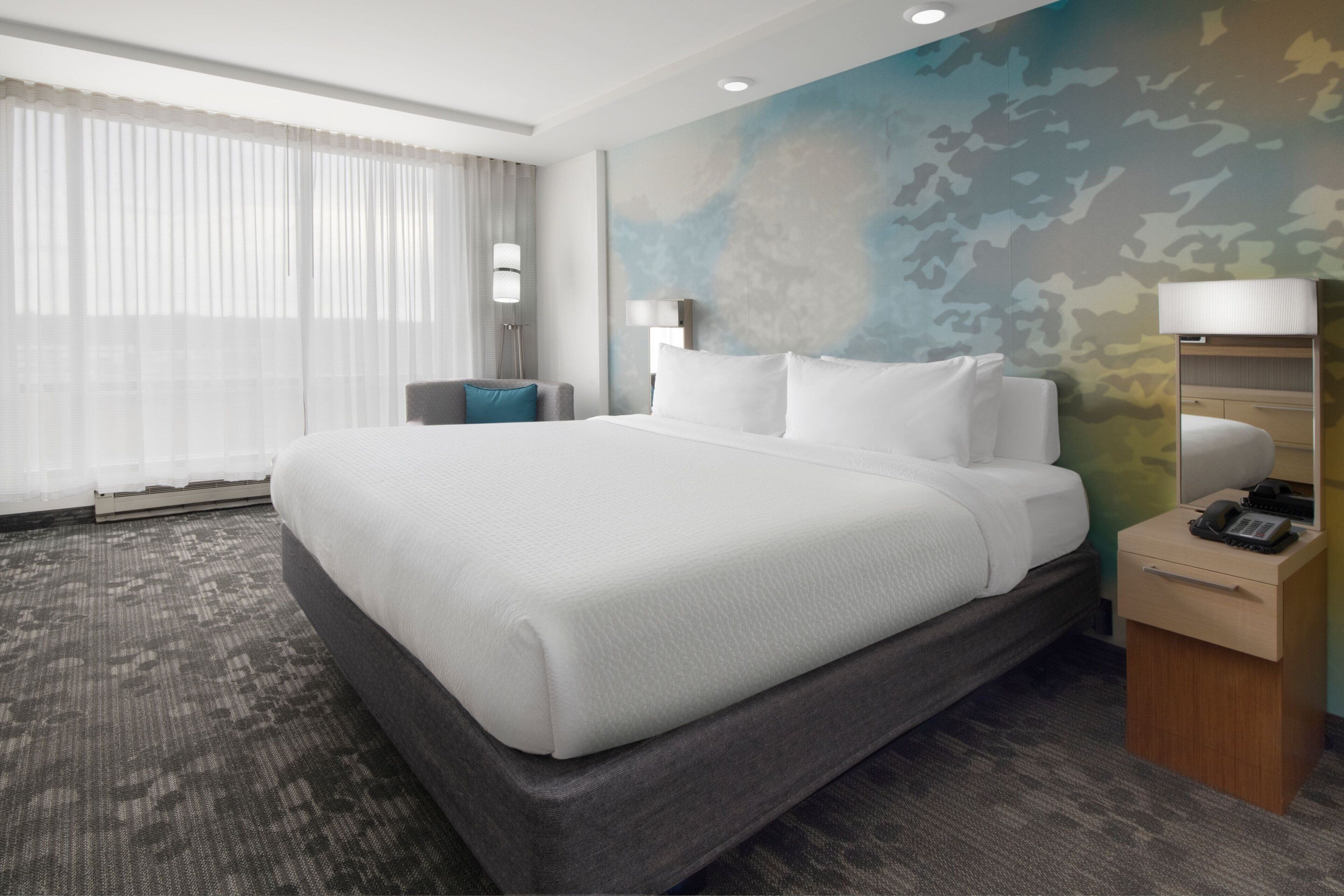 Une chambre d’hôtel avec un grand lit, un bureau avec un téléphone et un mur orné d’un motif de camouflage.
