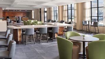 Un moderno vestíbulo de hotel con una zona de bar central, arreglos para sentarse y amplias ventanas que brindan luz natural.