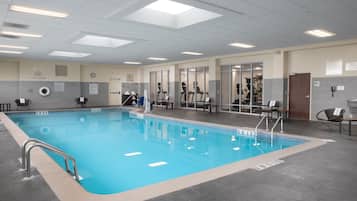An indoor swimming pool with clear water, surrounded by exercise equipment and seating areas.