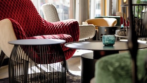Un área de estar moderna con una butaca tapizada de rojo, una silla blanca y una silla verde. Hay dos mesitas redondas con patas negras.