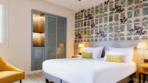 Habitación de hotel con una cama grande, un sillón amarillo, un armario y un papel tapiz con motivos florales.