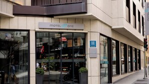 Un motel moderno con una amplia entrada de vidrio, un letrero que dice 'Motel One' y un número de habitación visible 'H 2200'.