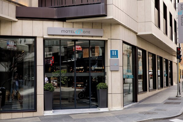 A modern motel with a large glass entrance, a sign reading "Motel One," and a visible room number "H 2200." - Motel One Madrid-Plaza de España (Madrid)