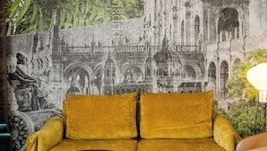 Una habitación con un sofá y dos mesitas auxiliares, un mural de un edificio histórico y una lámpara.