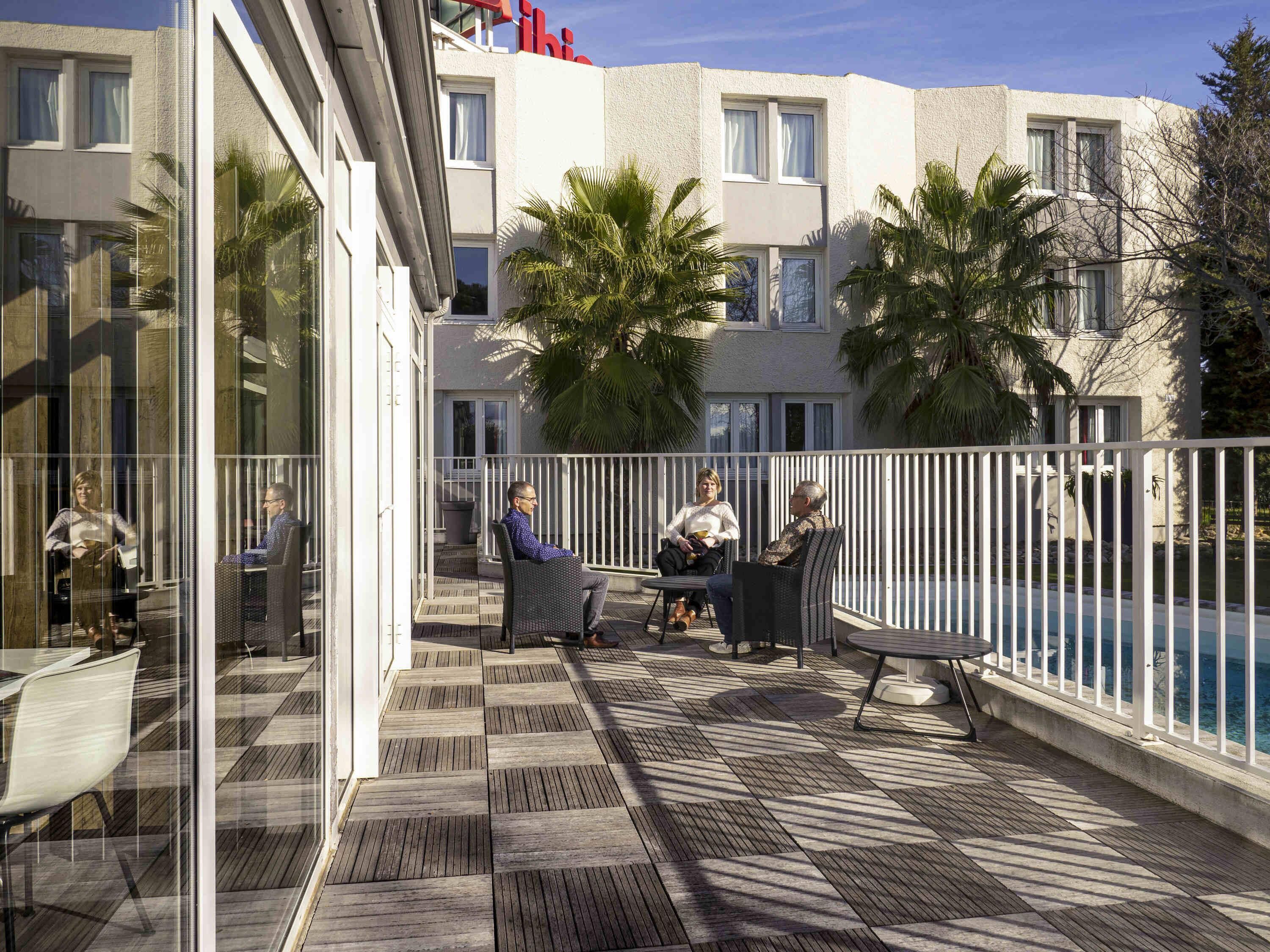 A rooftop patio with outdoor seating, a pool, and a building with a white facade and balconies.