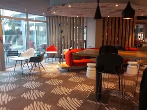 A modern interior with a mix of seating options, including a red sofa and multiple chairs, a patterned carpet, and a ceiling with artistic designs.