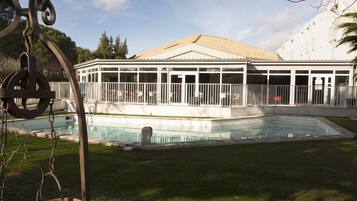 A pool area with a covered patio, a swing set, and a building with a tiled roof.