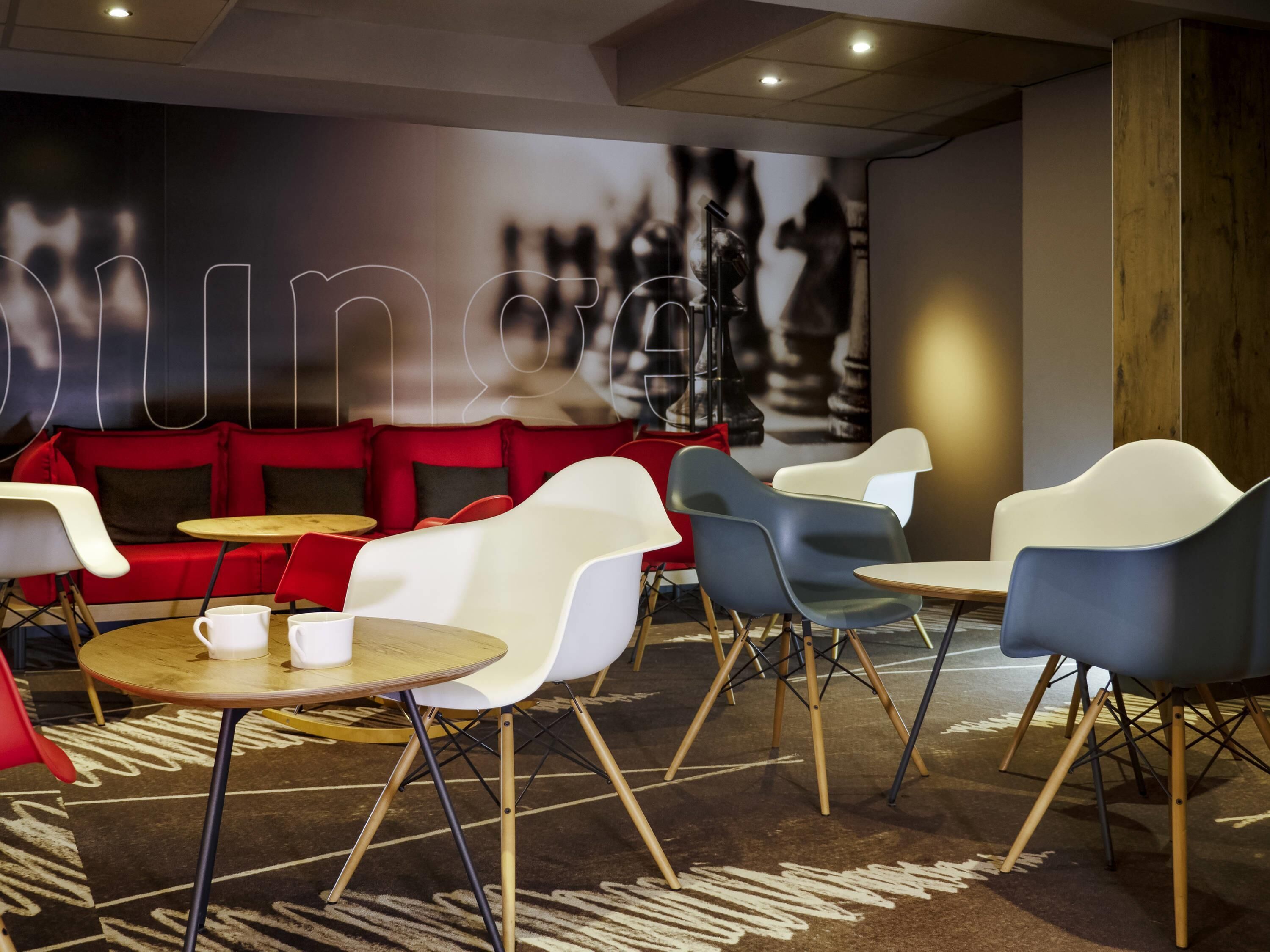 A modern lounge area with red seating, white and blue chairs, and small round tables.