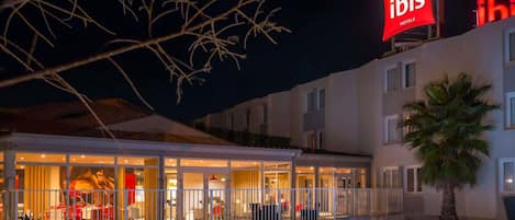 A hotel with a swimming pool, outdoor seating, and a prominent red sign.