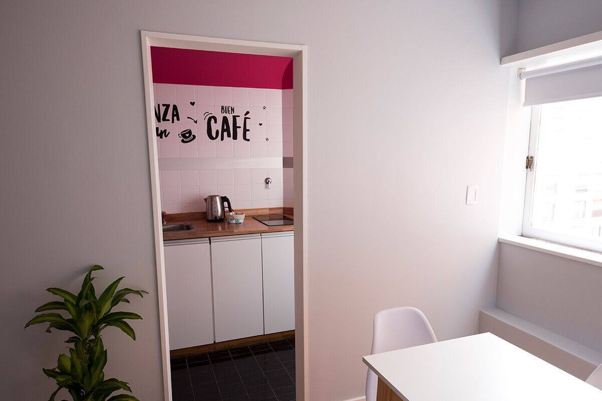 A small kitchen with white cabinets, a pink accent wall, and a window.