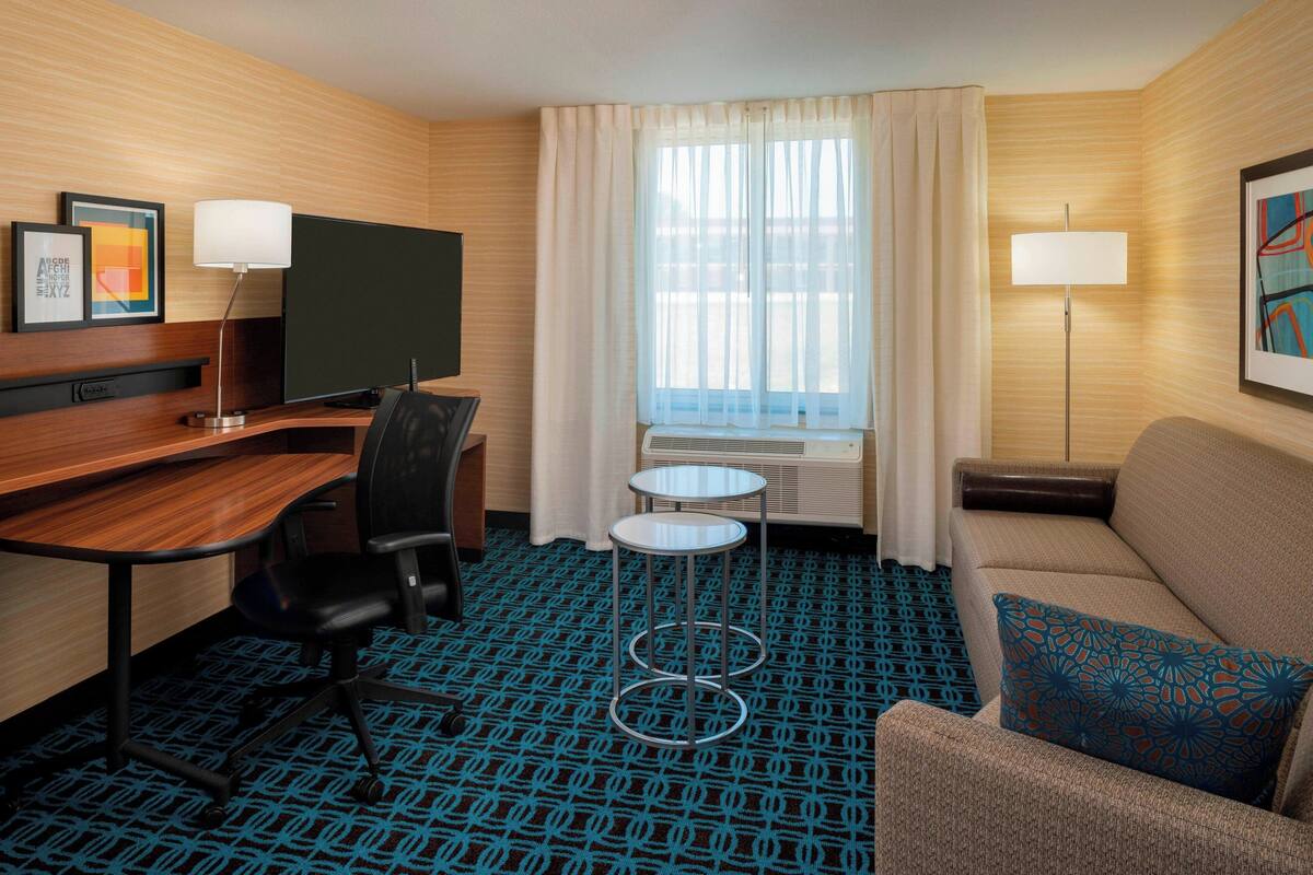Une chambre d’hôtel avec un bureau en bois, une télévision, un canapé, une petite table et une moquette à motifs.