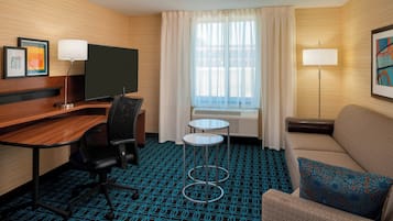 Une chambre d’hôtel avec un bureau en bois, une télévision, un canapé, une petite table et une moquette à motifs.