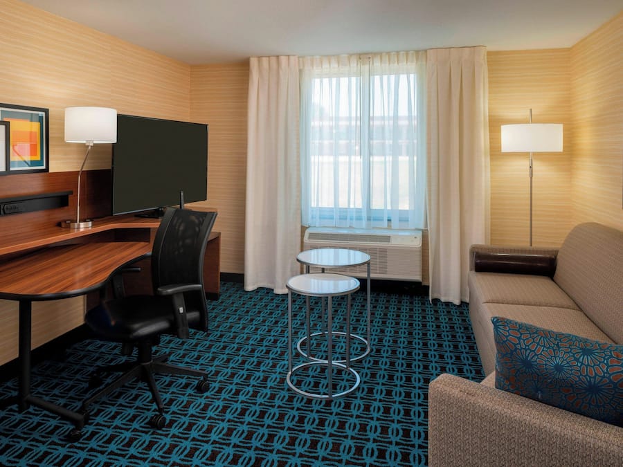Une chambre d’hôtel avec un bureau en bois, une télévision, un canapé, une petite table et une moquette à motifs.