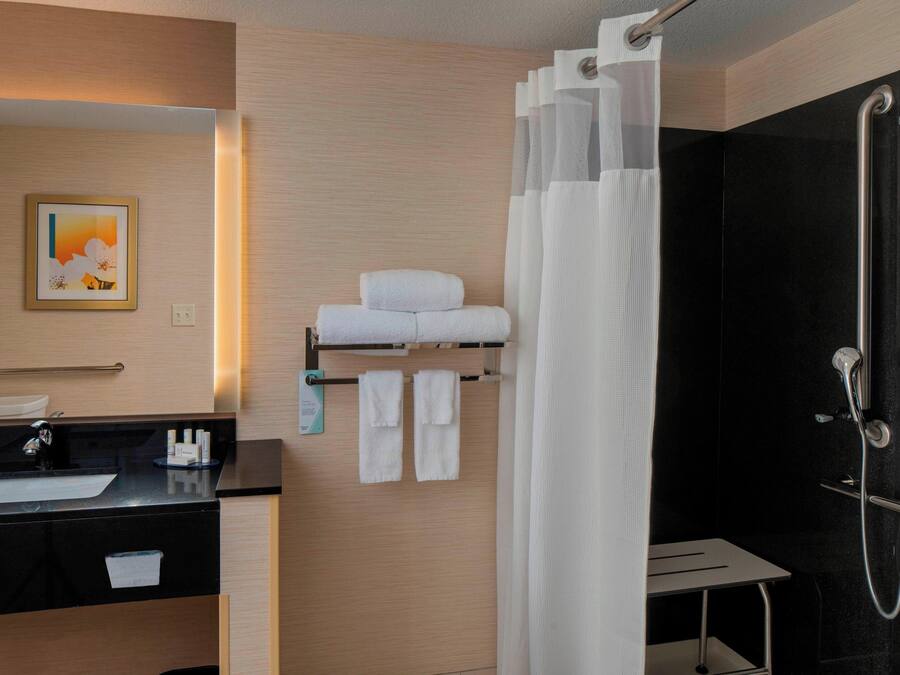 A modern bathroom with a black sink, white towels, a glass shower enclosure, and a framed picture on the wall.
