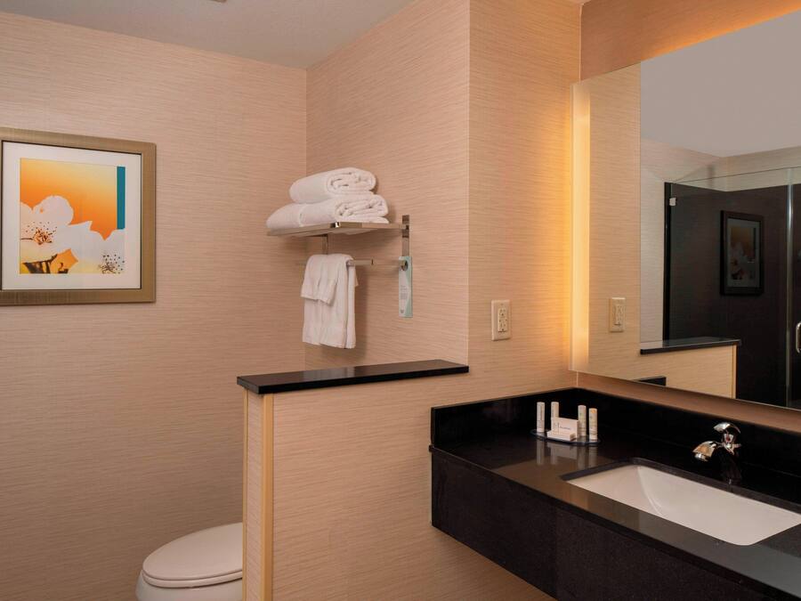 Un baño moderno con encimera negra, lavamanos blanco y un perchero para toallas.