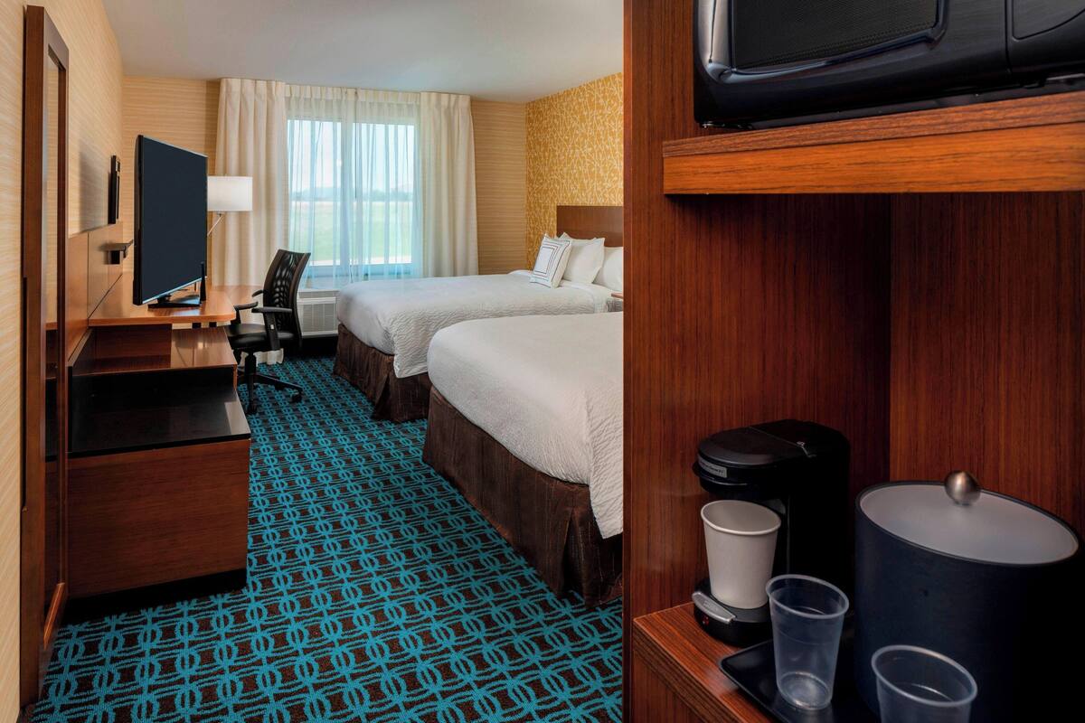 Une chambre d’hôtel avec deux lits, un bureau, une télévision, une machine à café et une moquette à motifs.