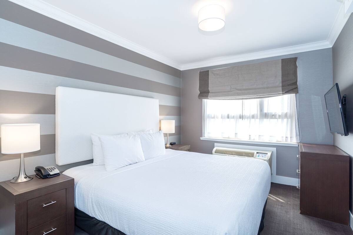 A hotel room with a large bed, bedside tables with lamps, a TV, and a window with curtains.
