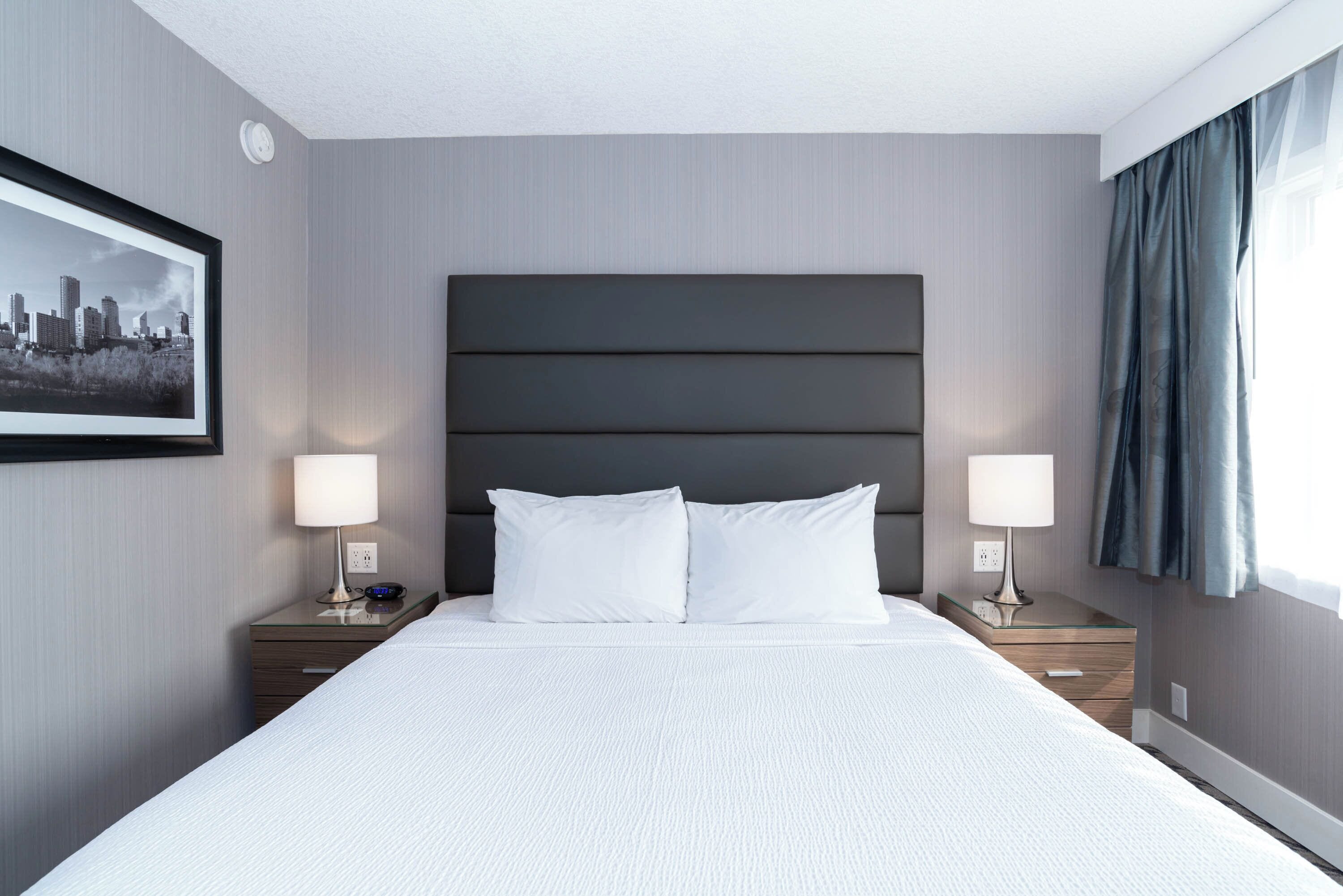 Ein Hotelzimmer mit einem großen Bett, zwei Nachttischen, einer Kopfteil und einem gerahmten Bild an der Wand.