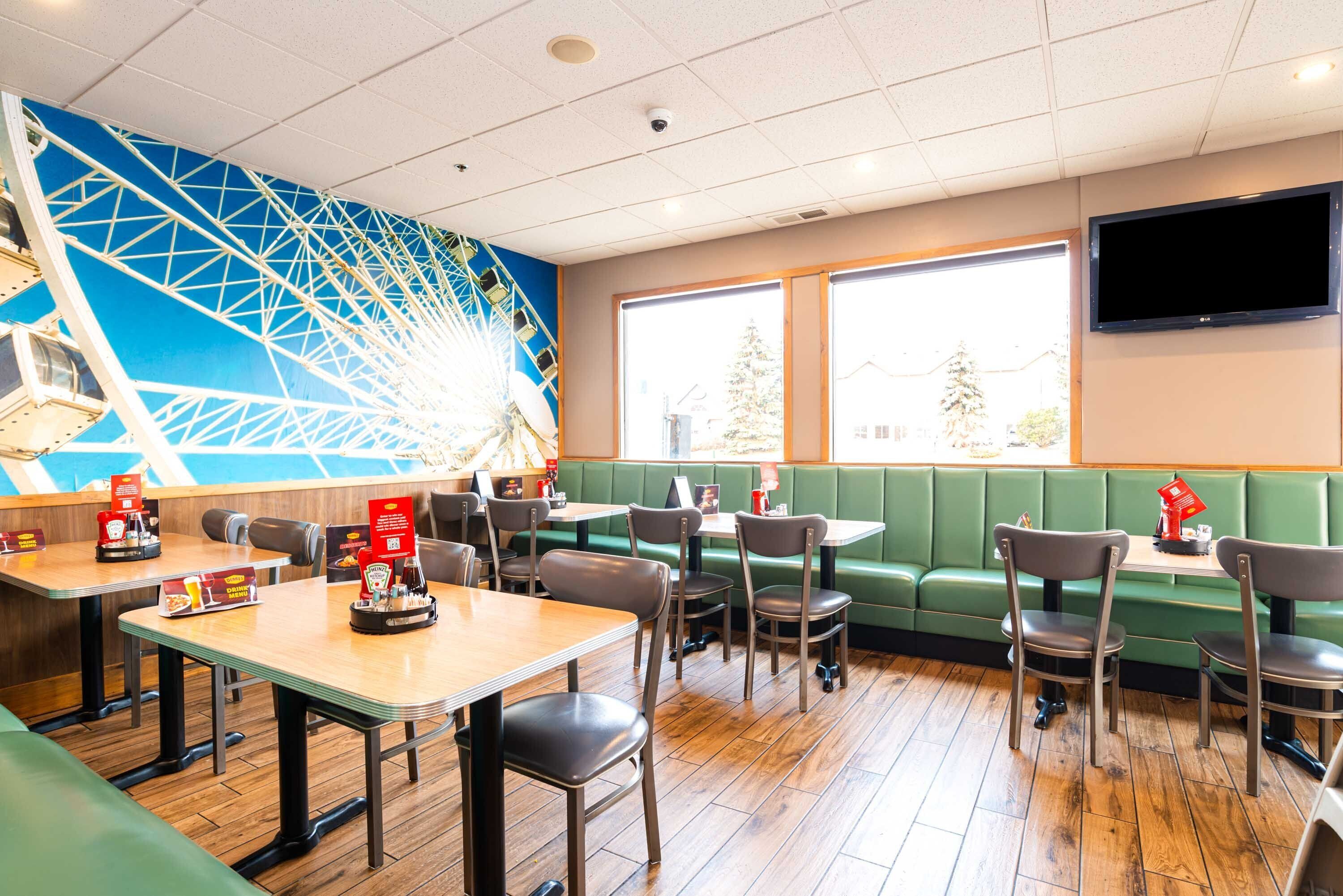 A restaurant with booths and tables, a large mural, and a TV on the wall.