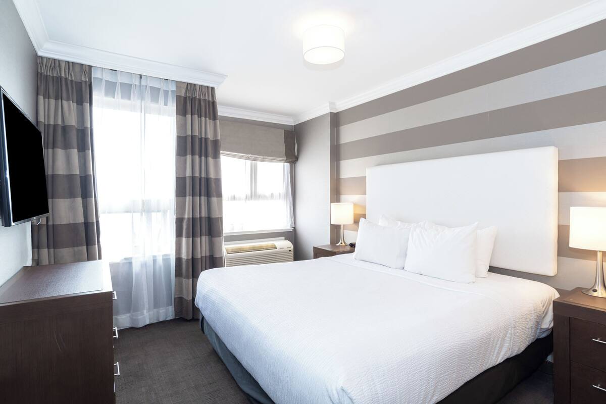 A hotel room with a large bed, a flat-screen TV, a desk, and a window with curtains.