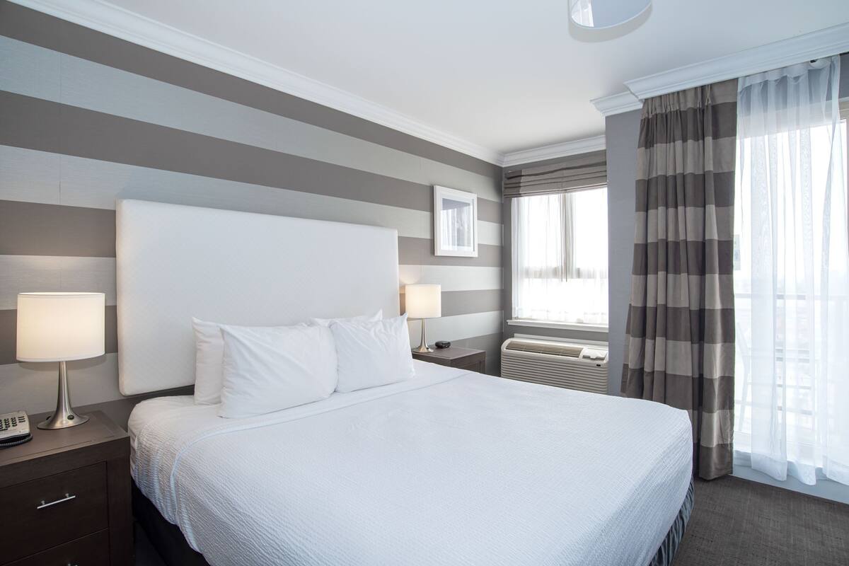 A hotel room with a large bed, two bedside tables with lamps, a framed picture on the wall, and a window with curtains.