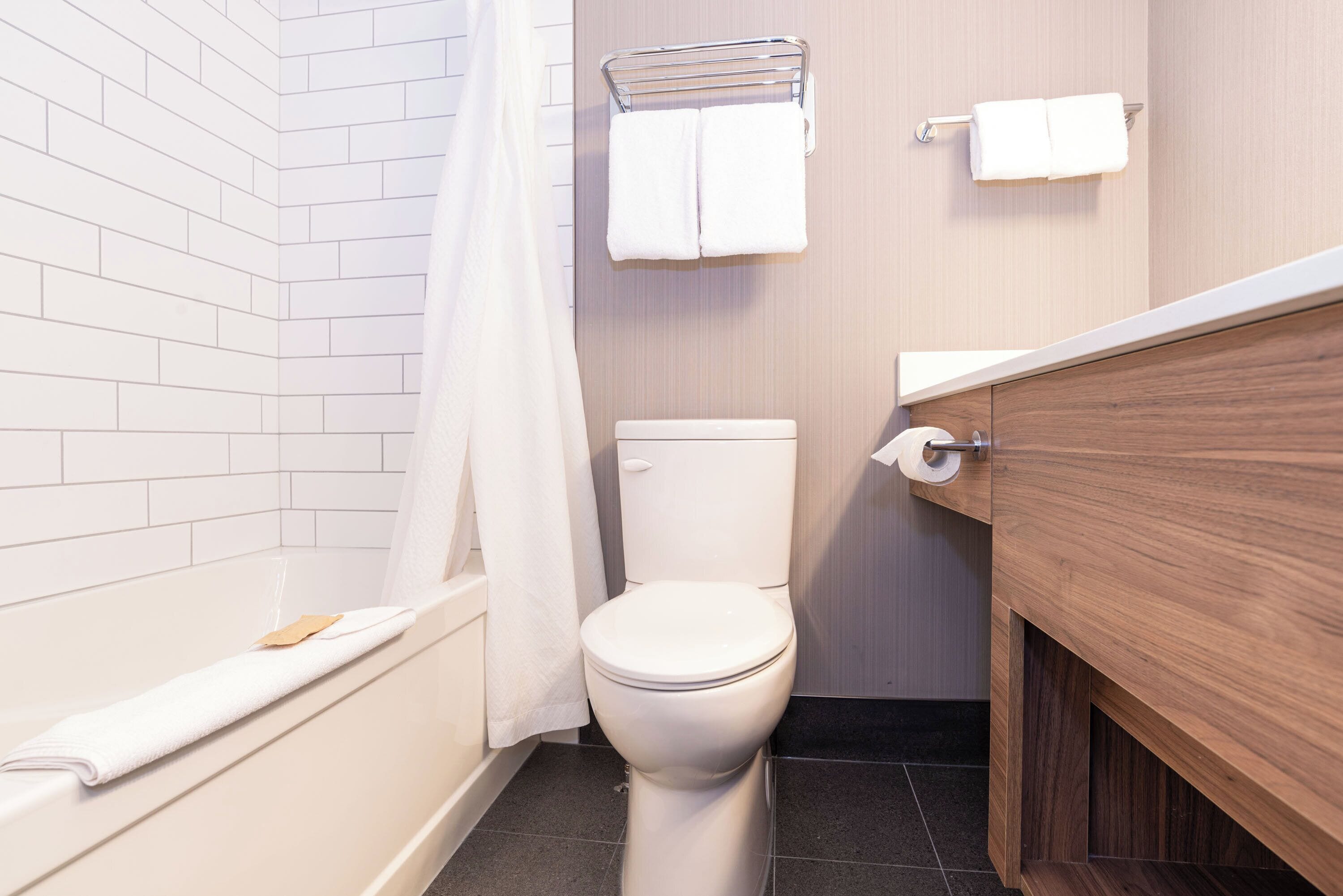 Un baño con inodoro blanco, una bañera con detalle de madera y un perchero con dos toallas.