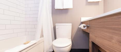 Un baño con inodoro blanco, una bañera con detalle de madera y un perchero con dos toallas.