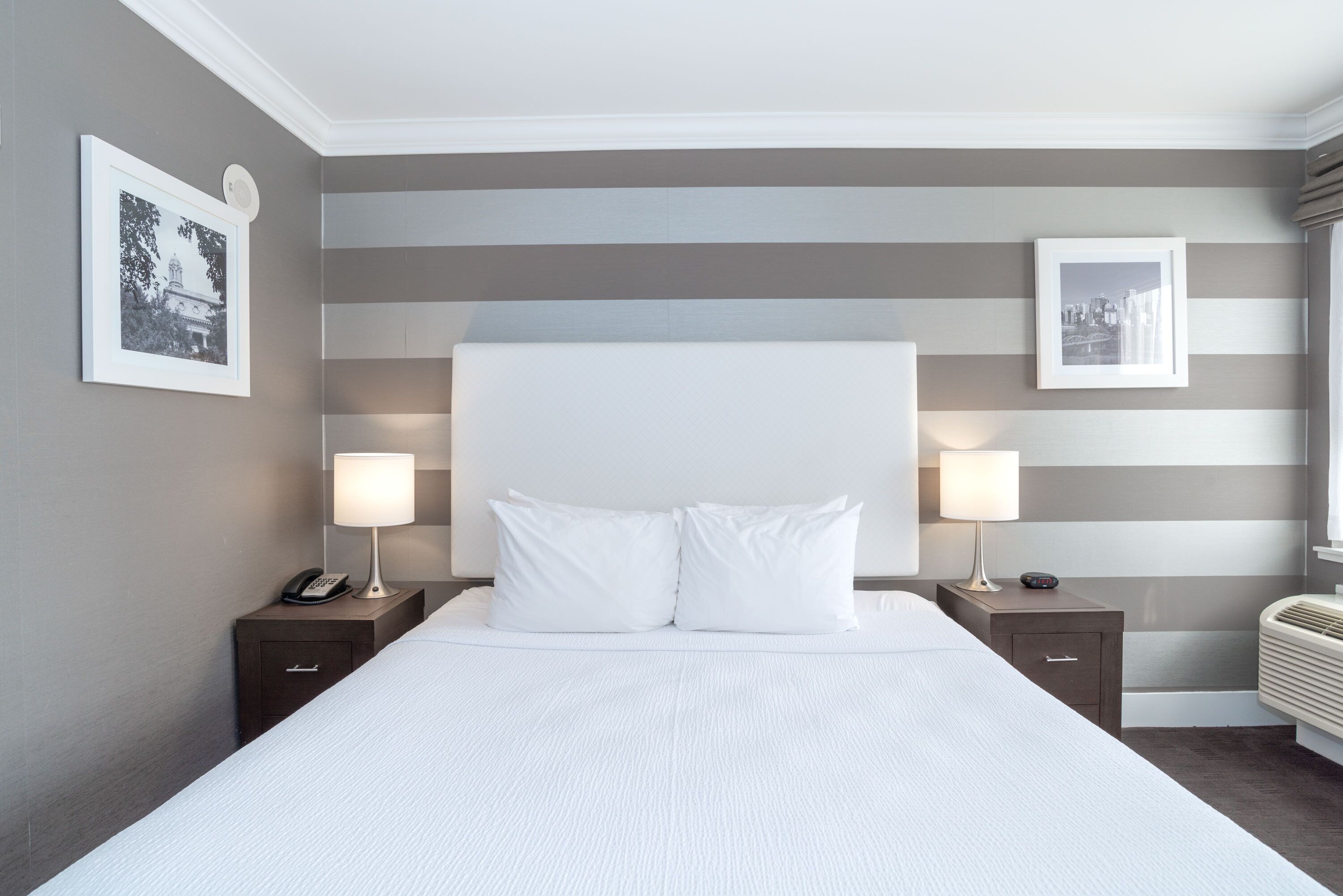 A hotel room with a large bed, two bedside tables with lamps, and striped wall decor.