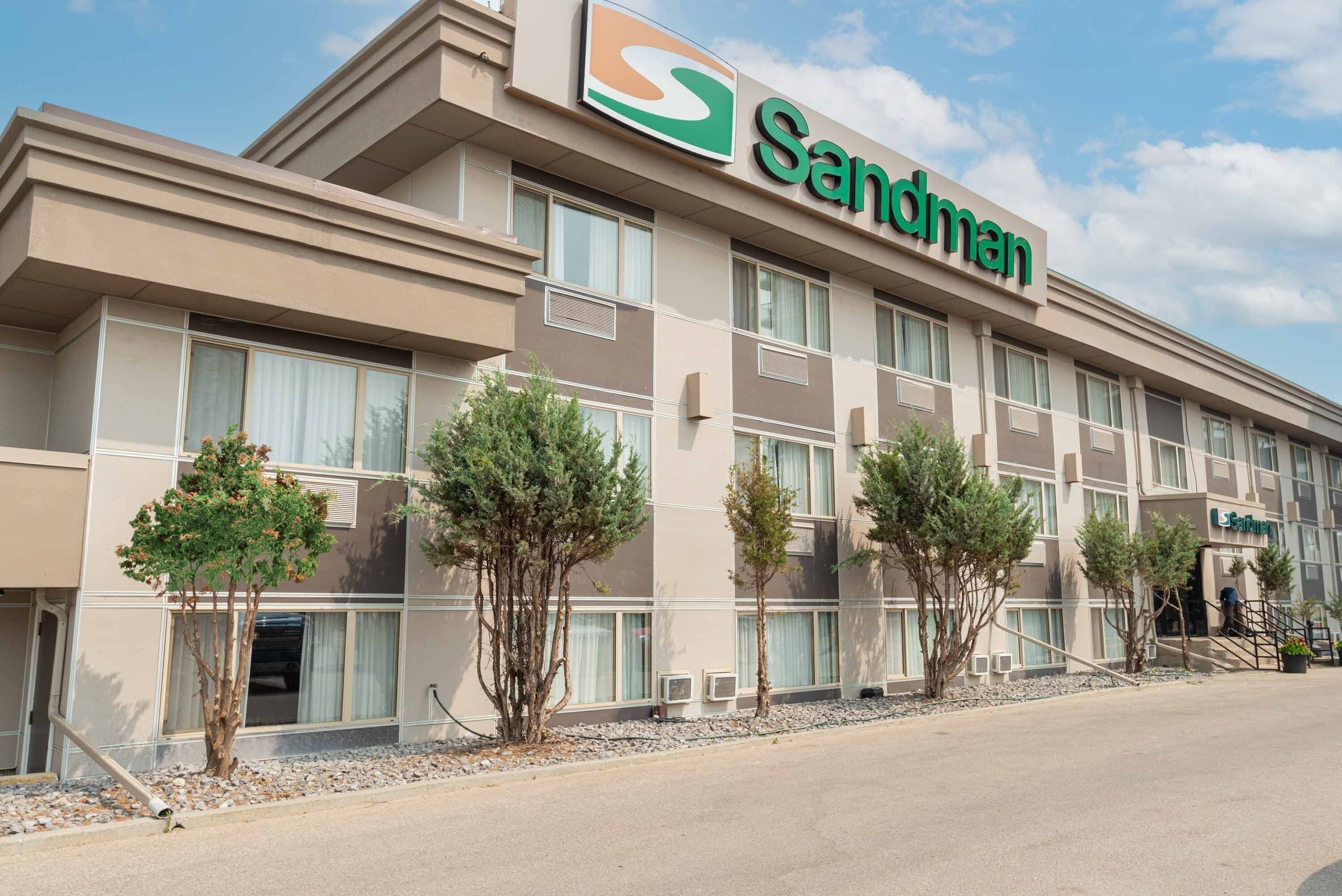 Un hotel Sandman con una fachada moderna, múltiples ventanas y unos pocos árboles pequeños al frente.