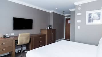 A hotel room with a bed, a desk with a chair, a flat-screen TV, a wardrobe, and a framed picture on the wall.
