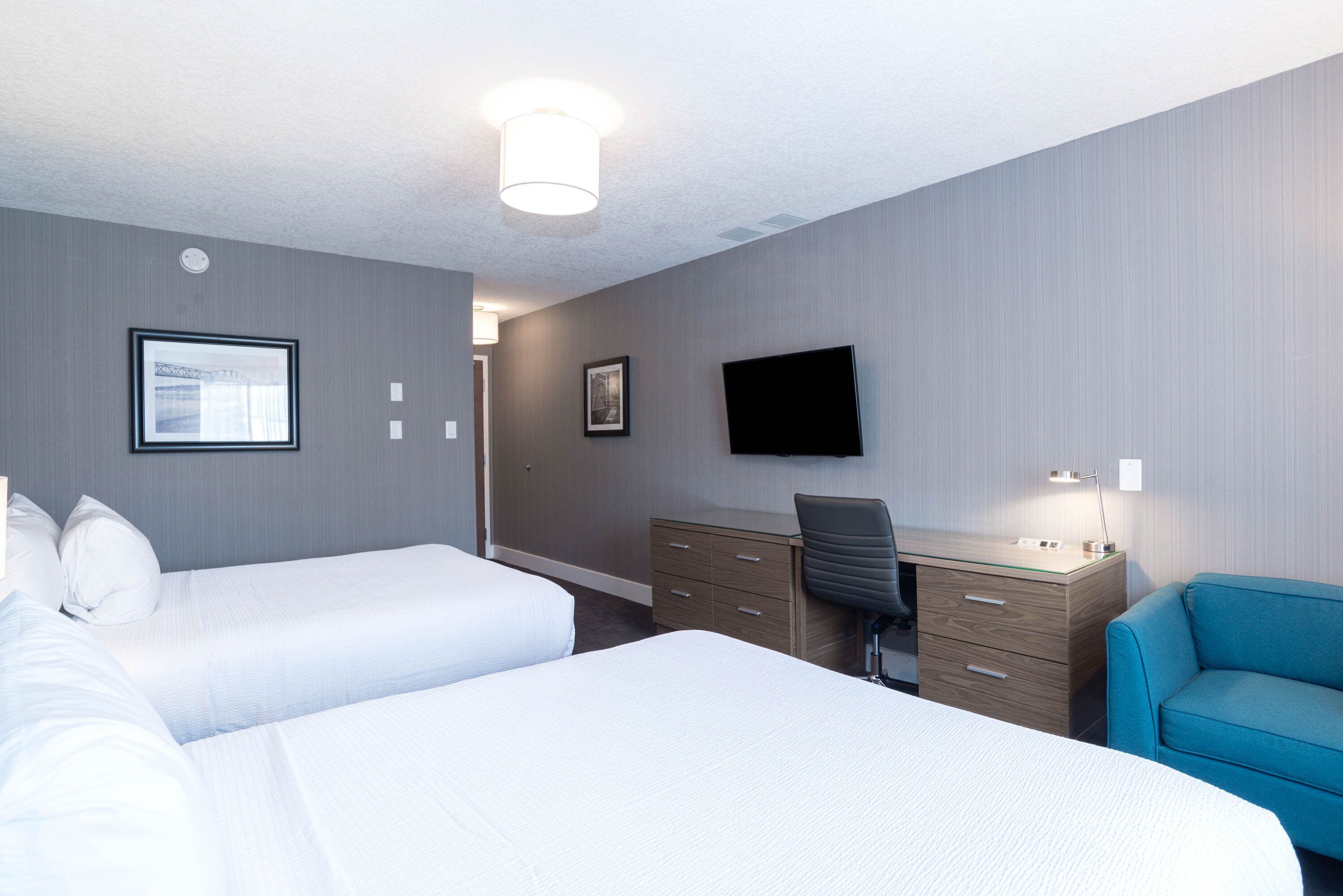 A hotel room with two beds, a desk, a chair, a TV, and a blue sofa.