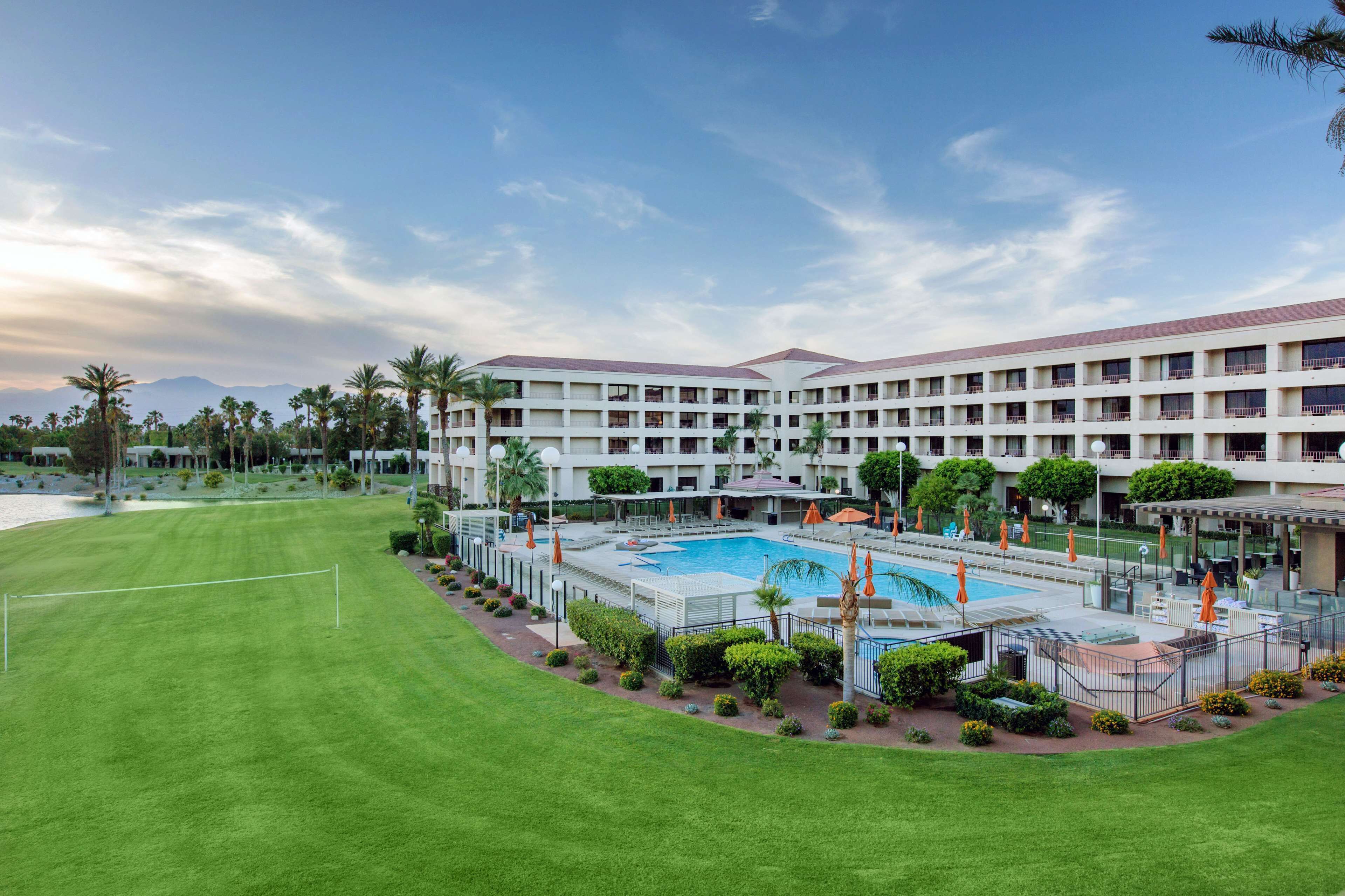 A hotel with a large pool, multiple floors, and a well-maintained lawn.