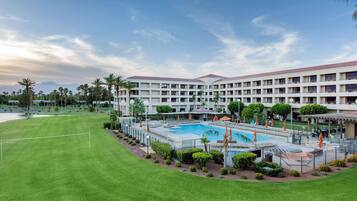 A hotel with a large pool, multiple floors, and a well-maintained lawn.