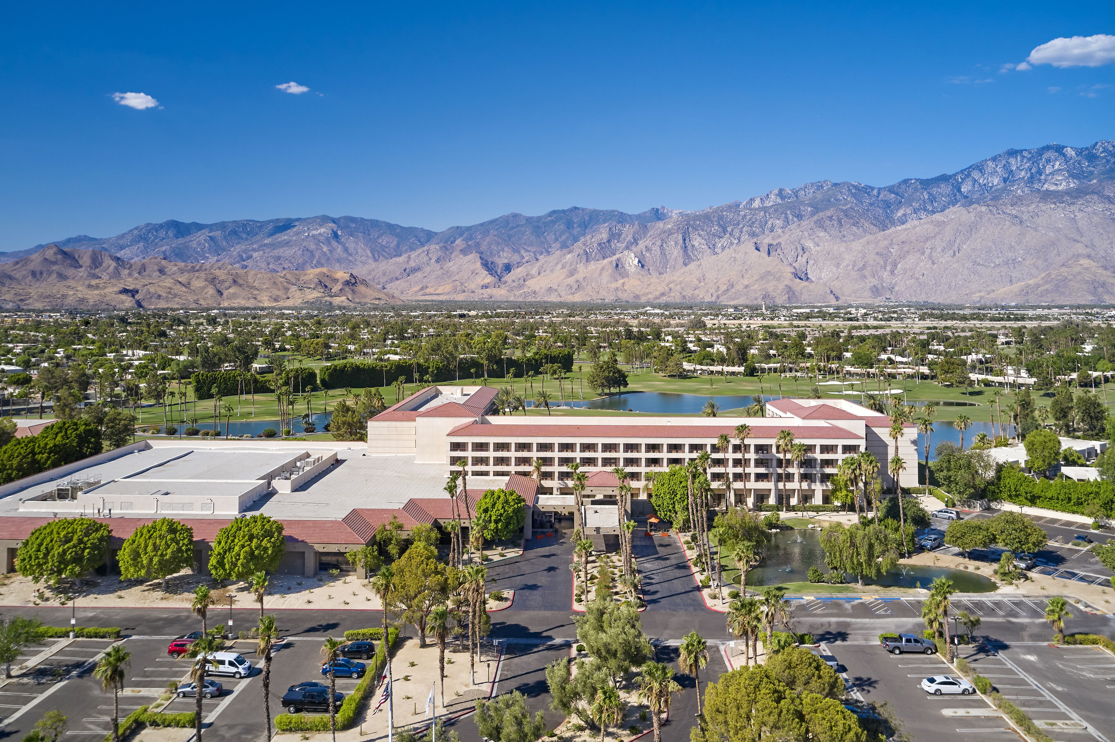 A large hotel with multiple floors, a parking lot, and a view of mountains in the background.