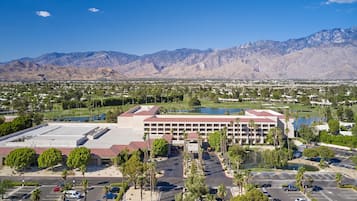 A large hotel with multiple floors, a parking lot, and a view of mountains in the background.