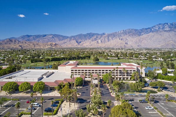 A large hotel with multiple floors, a parking lot, and a view of mountains in the background.