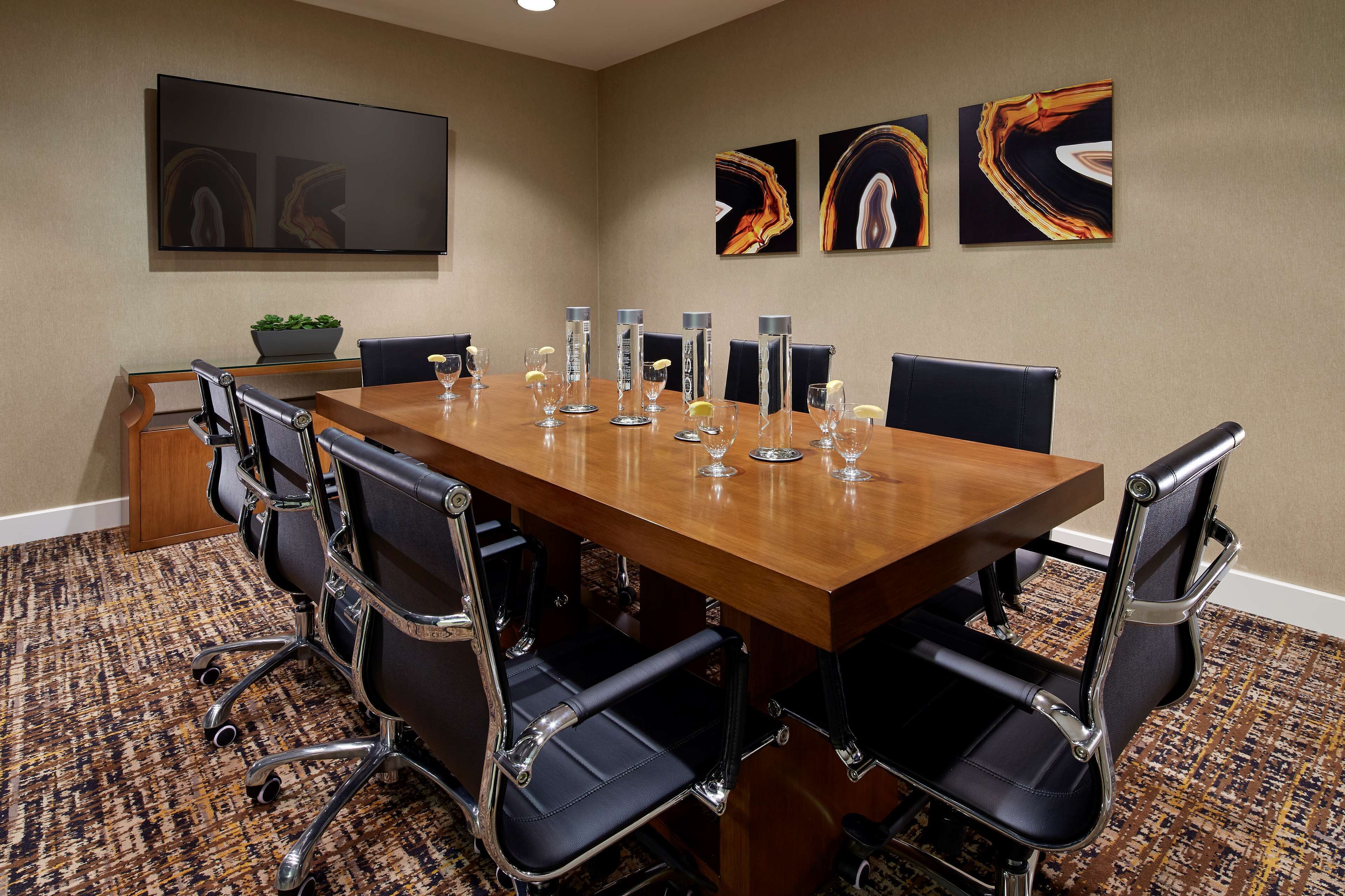 A conference room with a long wooden table, black leather chairs, and a patterned carpet.
