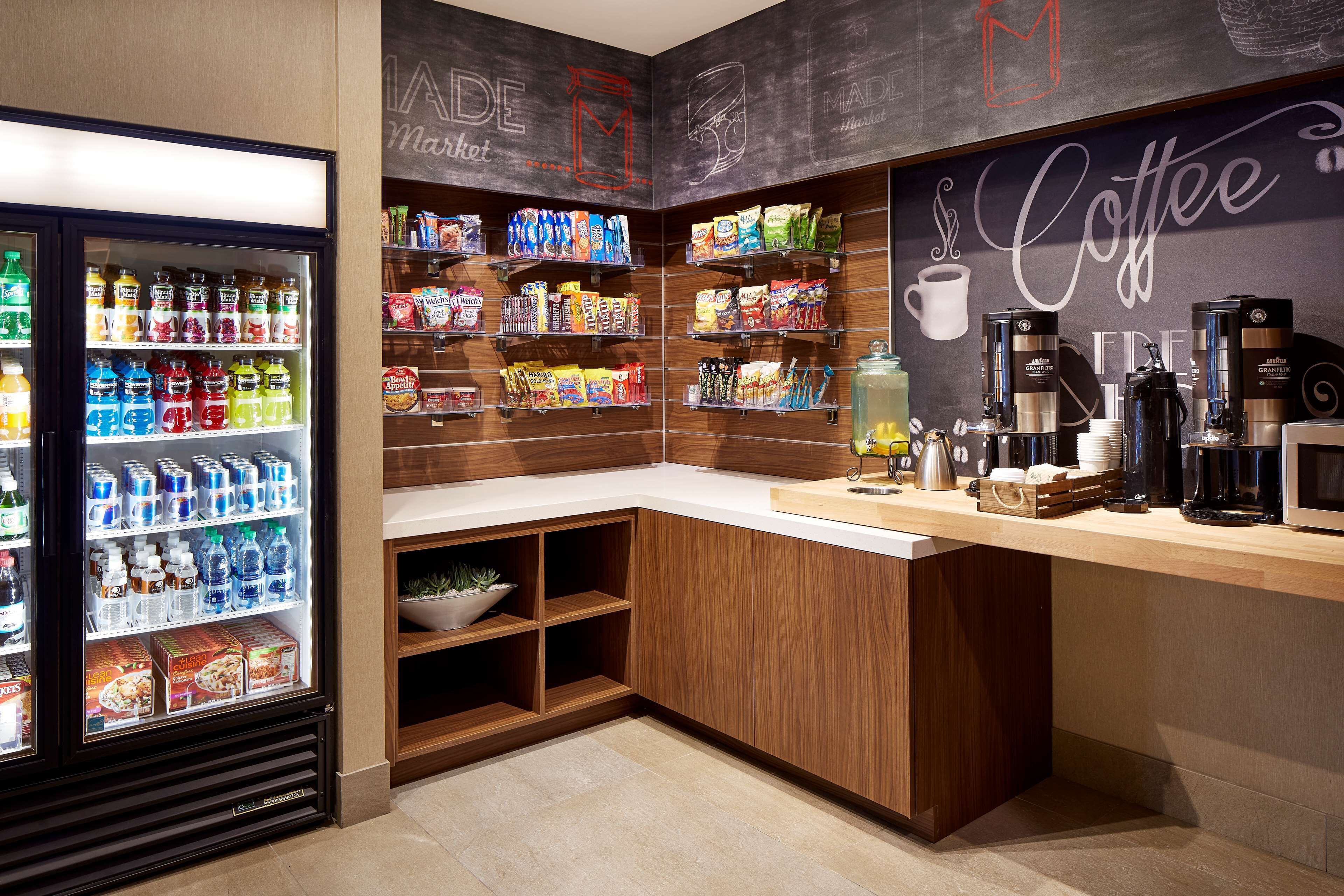 A coffee shop with a refrigerated beverage display, shelves stocked with snacks, and coffee-making equipment.