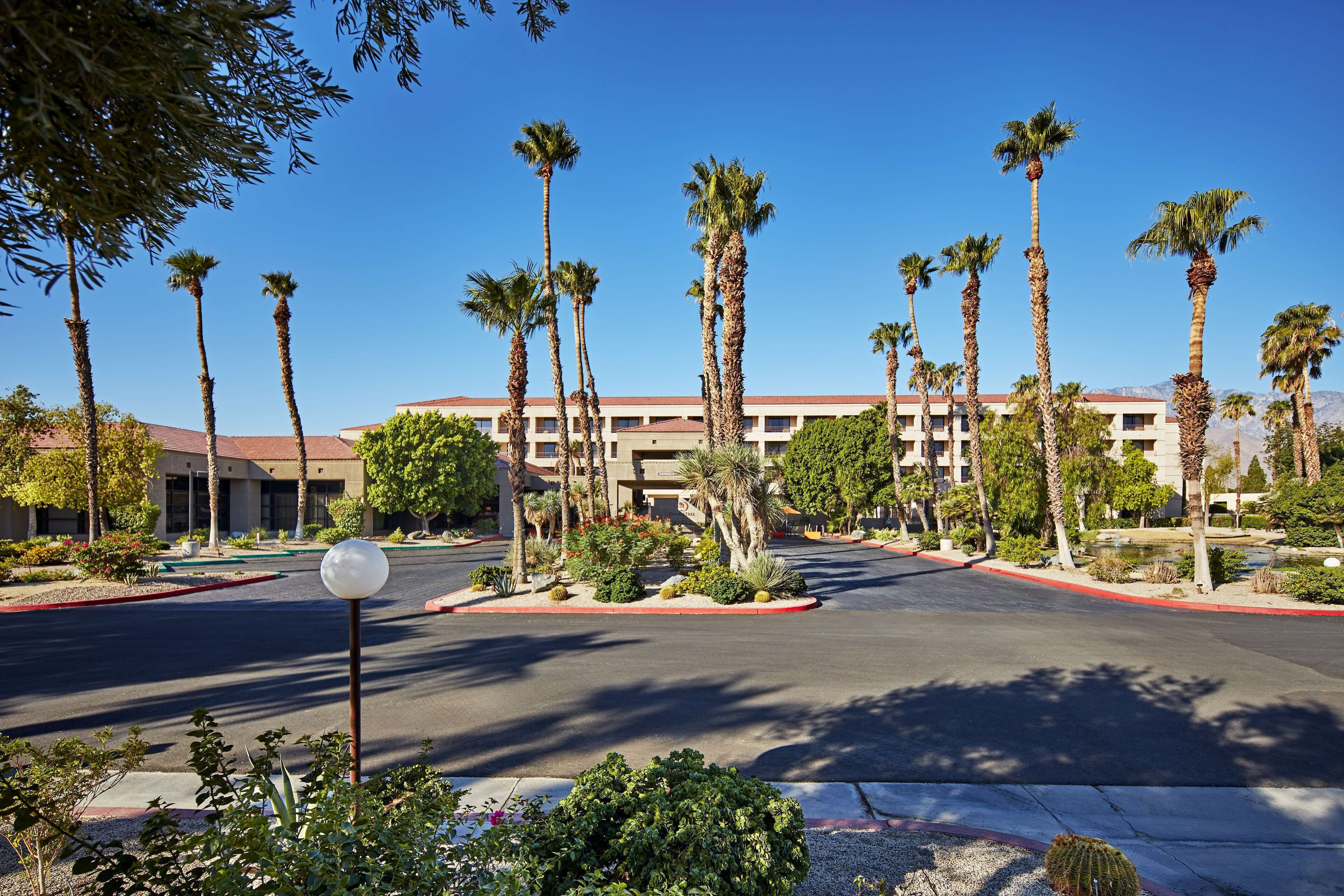 A hotel with a parking lot, palm trees, and a building with a red roof.