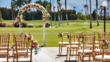 Hochzeitliche Zeremonie mit in Reihen angeordneten Stühlen, einem Blumenschmuckbogen und Blick auf einen Golfplatz im Hintergrund.