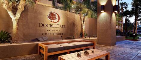 A DoubleTree by Hilton Golf Resort outdoor seating area with a stone wall, palm trees, and a wooden bench.