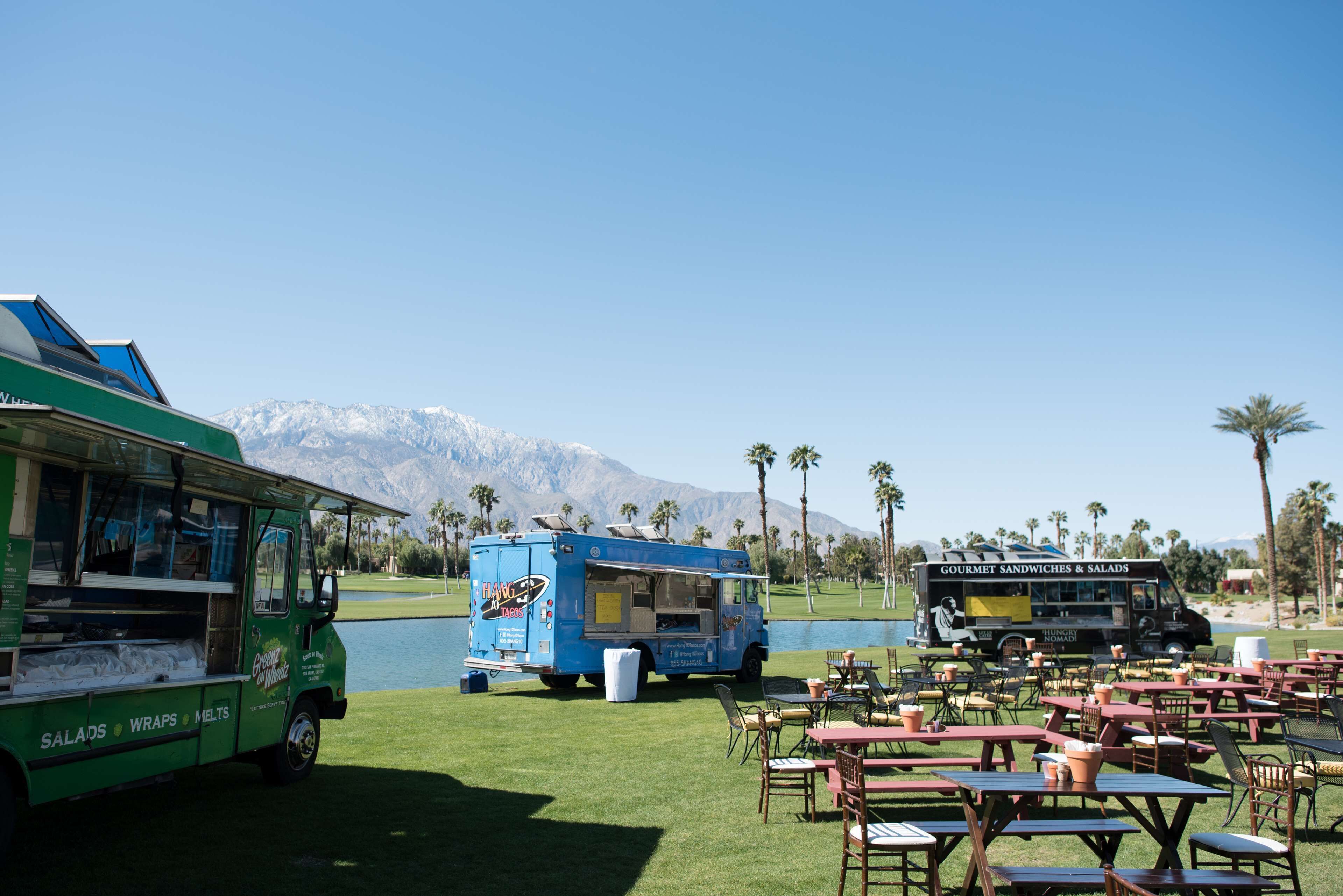 A food truck area with tables and chairs, a lake, and mountains in the background.