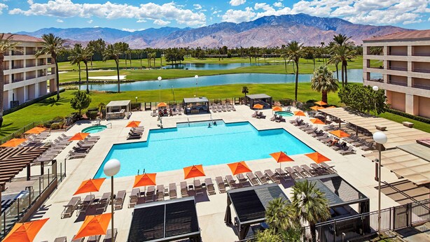 A resort pool area with multiple sun loungers and umbrellas, a central swimming pool, and a view of mountains in the background. - DoubleTree by Hilton Hotel Golf Resort Palm Springs (Cathedral City)