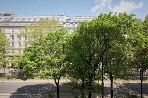 A street view with a row of trees in the foreground and a row of buildings in the background.