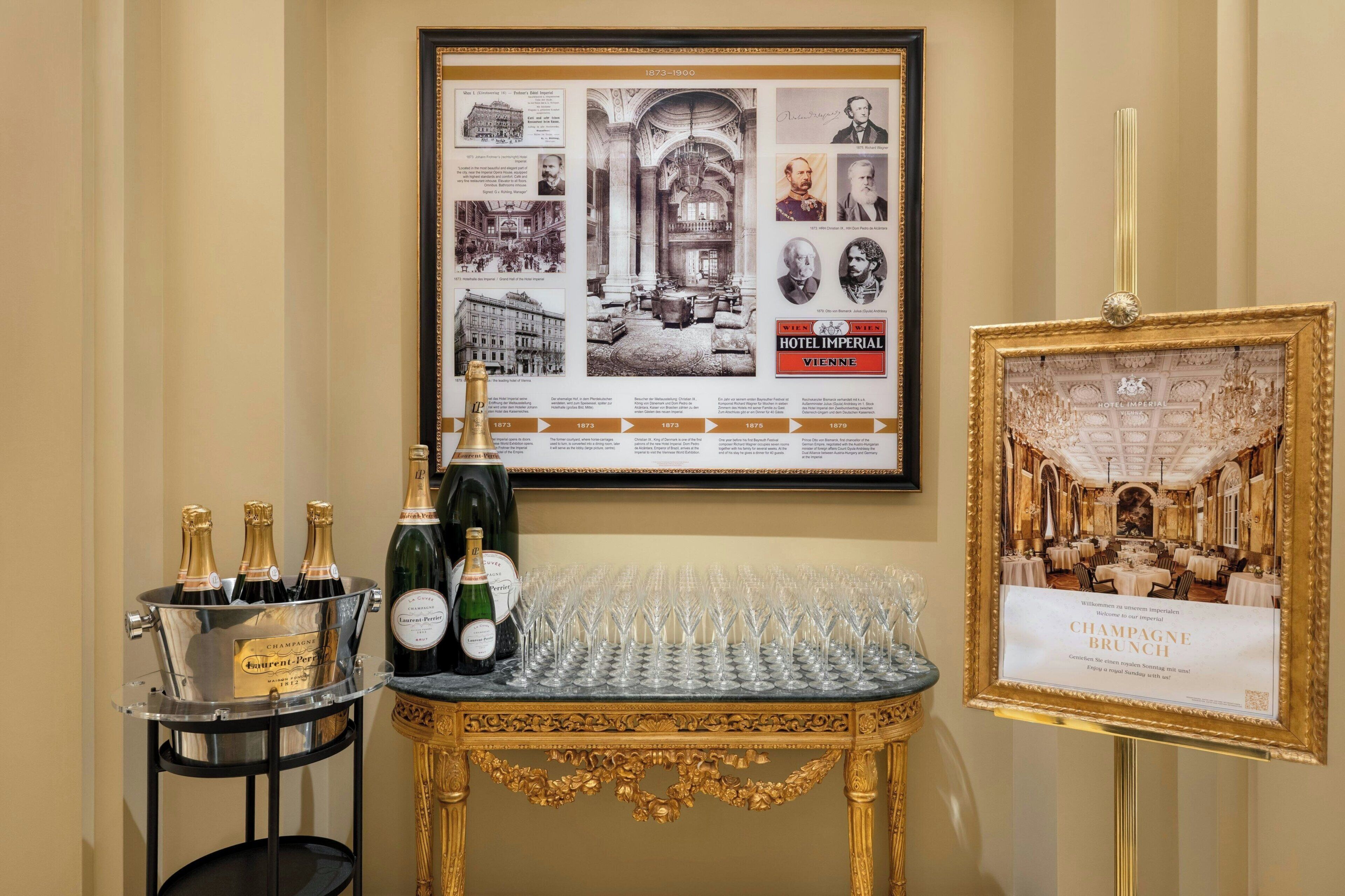 A framed historical photo of Hotel Imperial Vienna, a display of champagne bottles and glasses, and a decorative table.