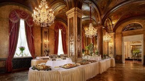 Een statige balzaal met weelderige kroonluchters, een lange eettafel gedekt voor een formeel evenement, en klassieke architectonische details.