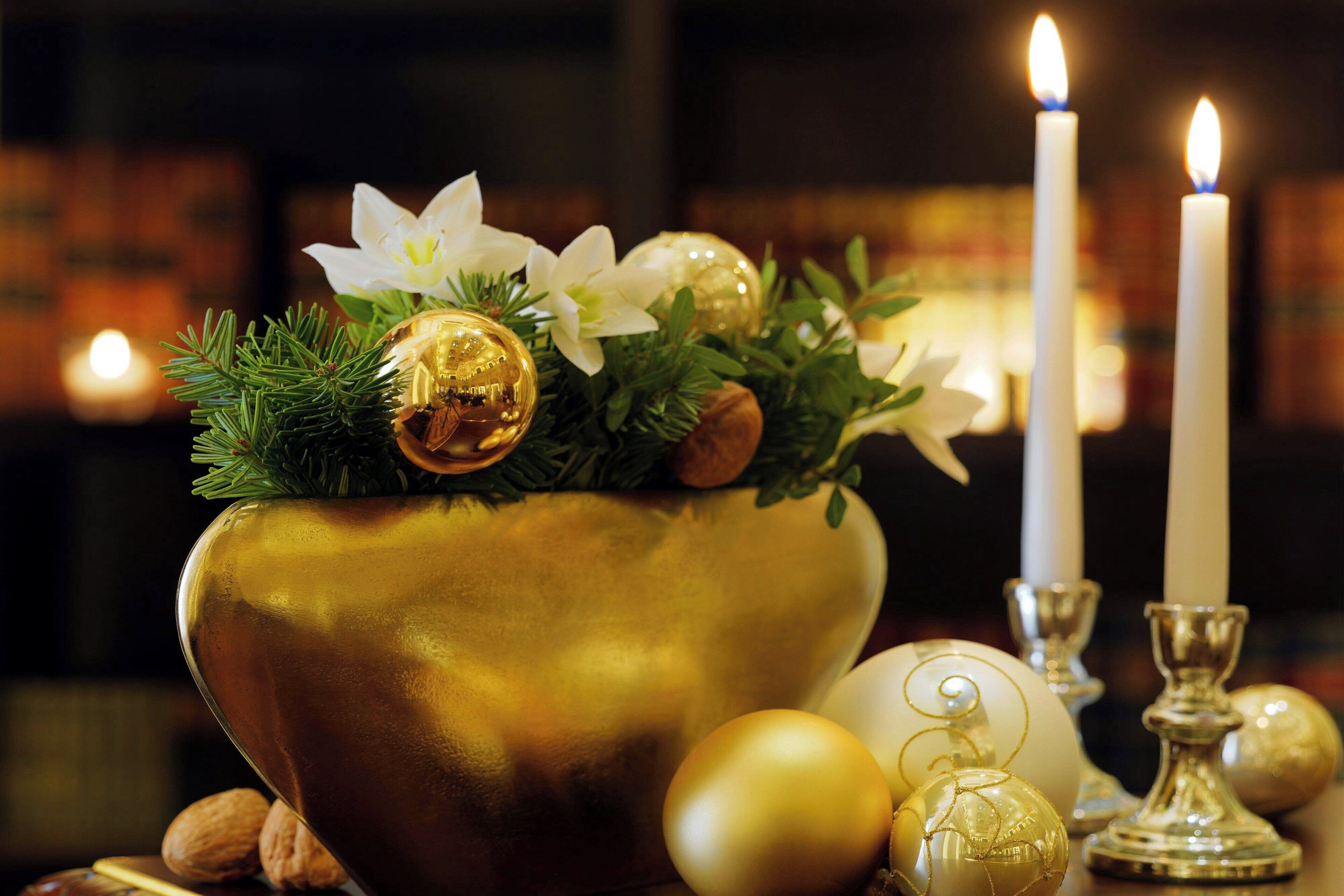 A decorative arrangement with a golden bowl, white candles, and golden ornaments.