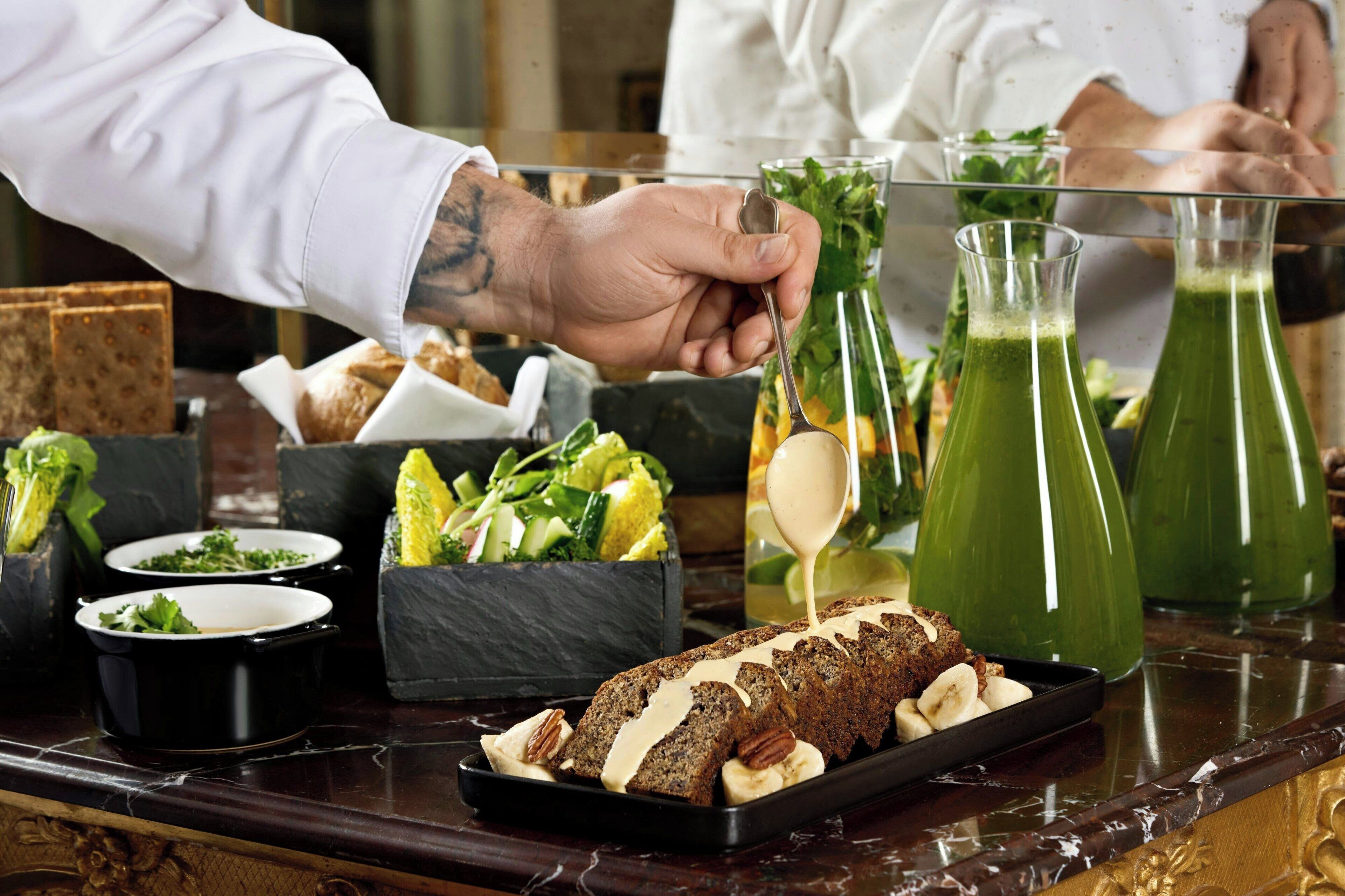 Una persona sirviendo comida en una mesa con varios platos, incluyendo un pan y bebidas verdes.